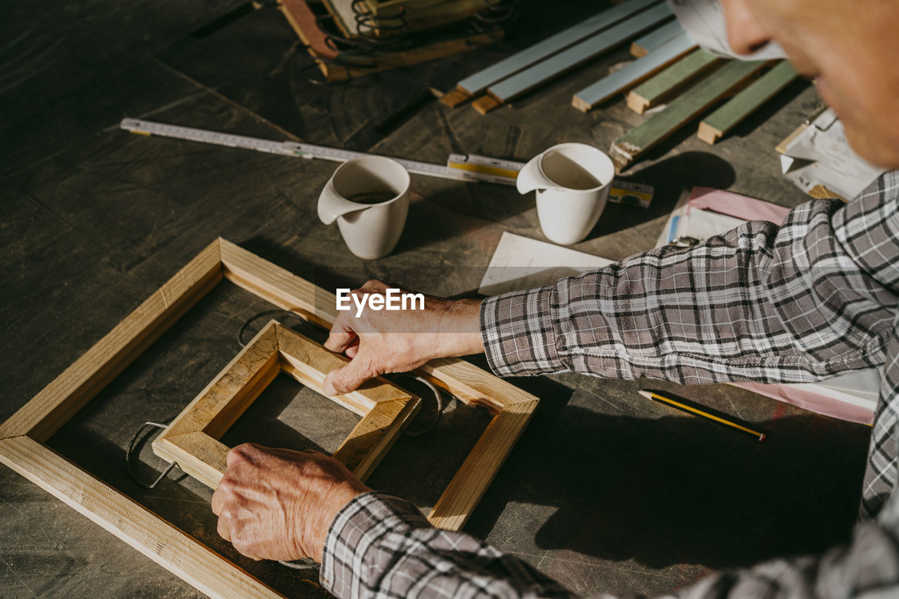 High angle view of senior craftsman making wooden frame at workshop