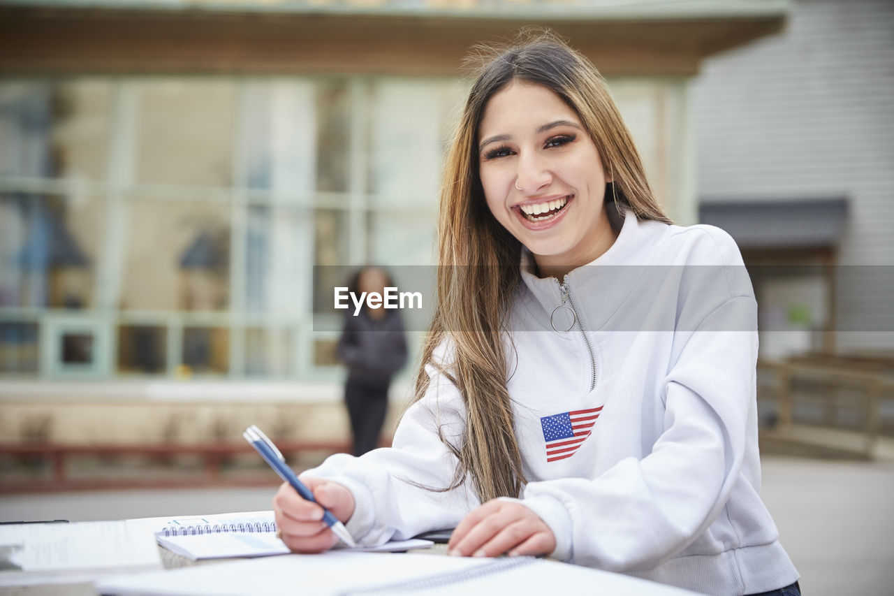 Portrait of smiling teenage girl sitting at table in schoolyard