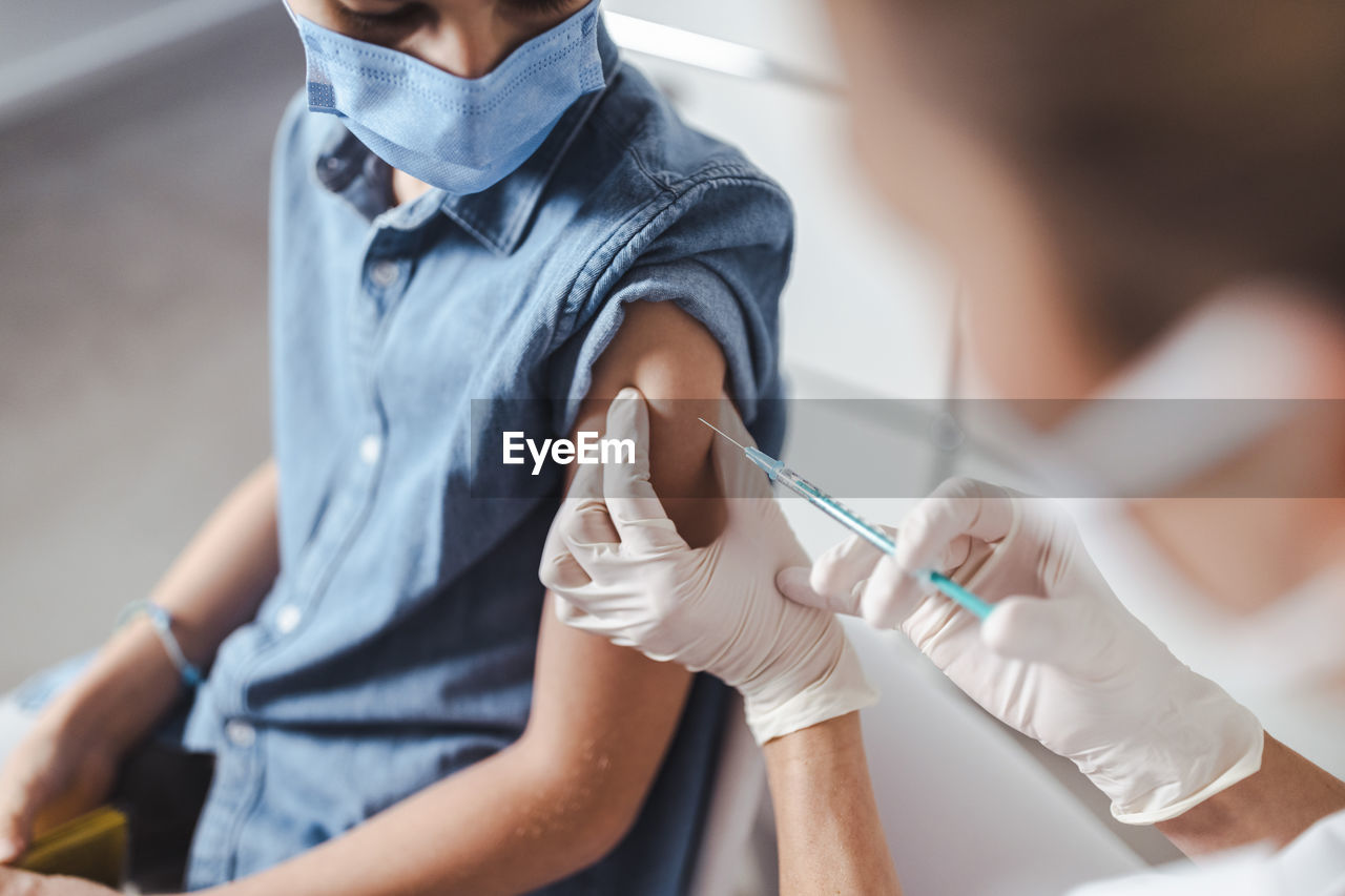 Nurse vaccinating boy with face mask at healthcare center