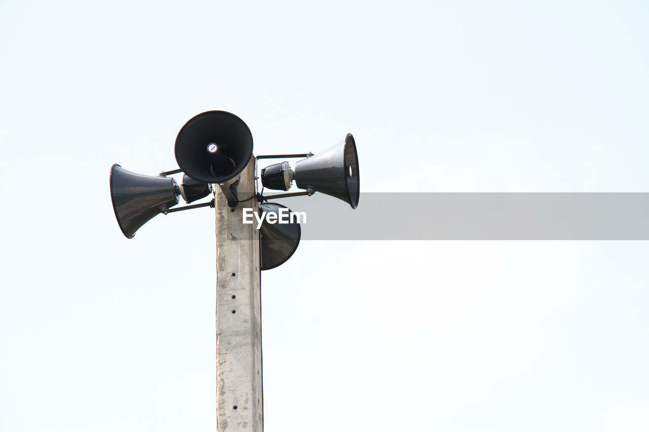 Low angle view of megaphones on pole against blue sky