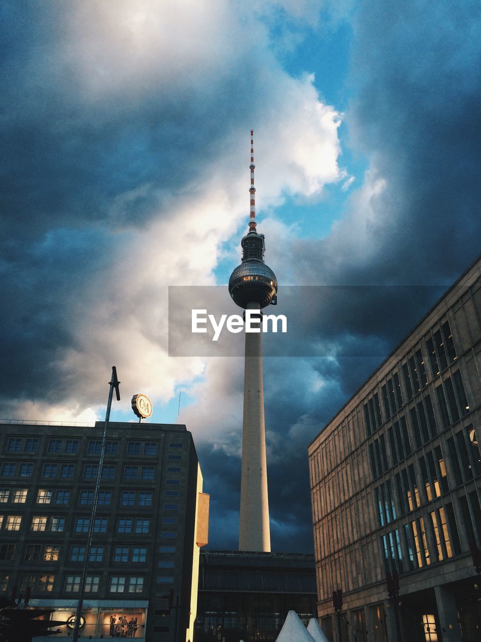 Low angle view of fernsehturm and buildings against cloudy sky