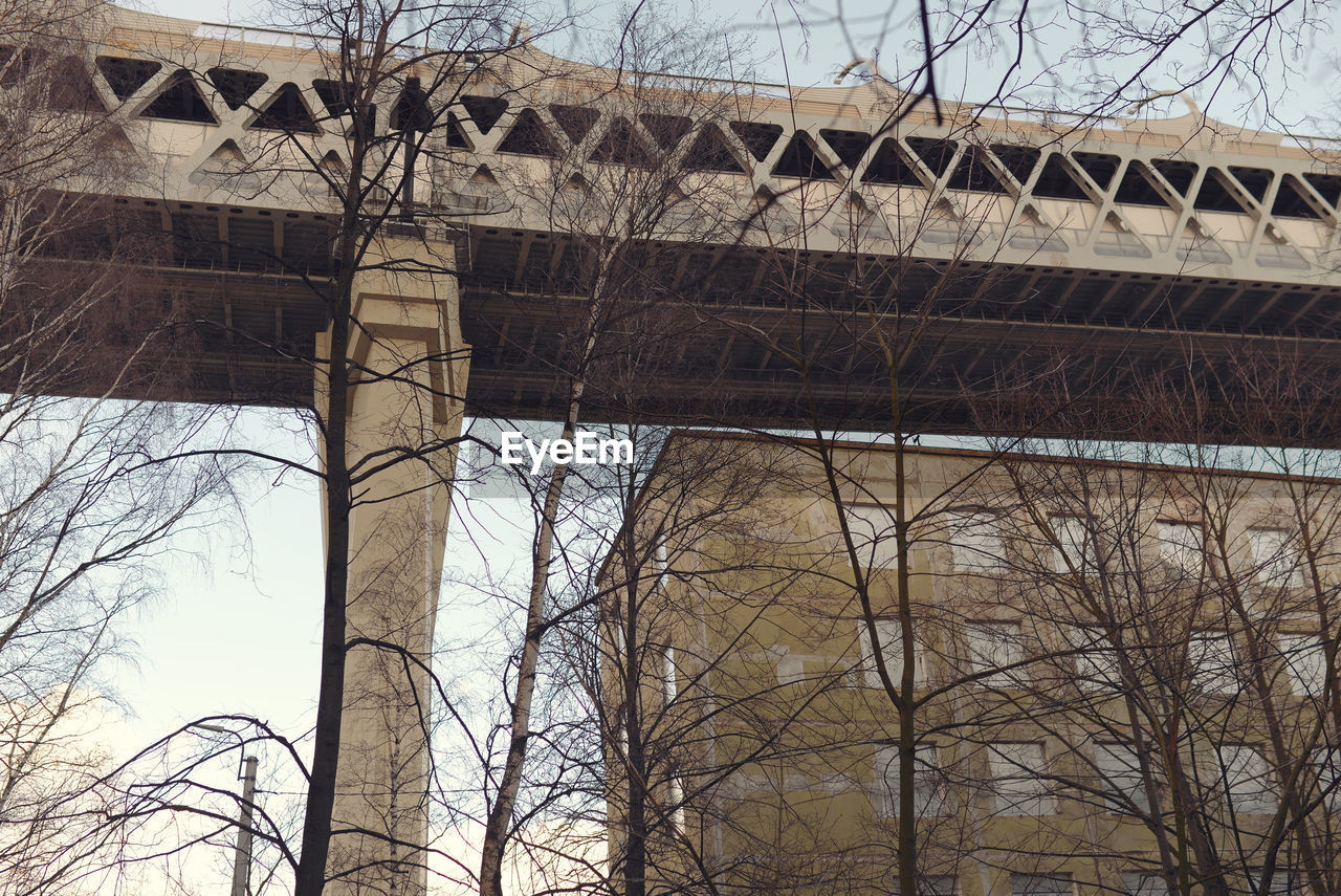 LOW ANGLE VIEW OF BRIDGE AND BARE TREES AGAINST BUILDINGS