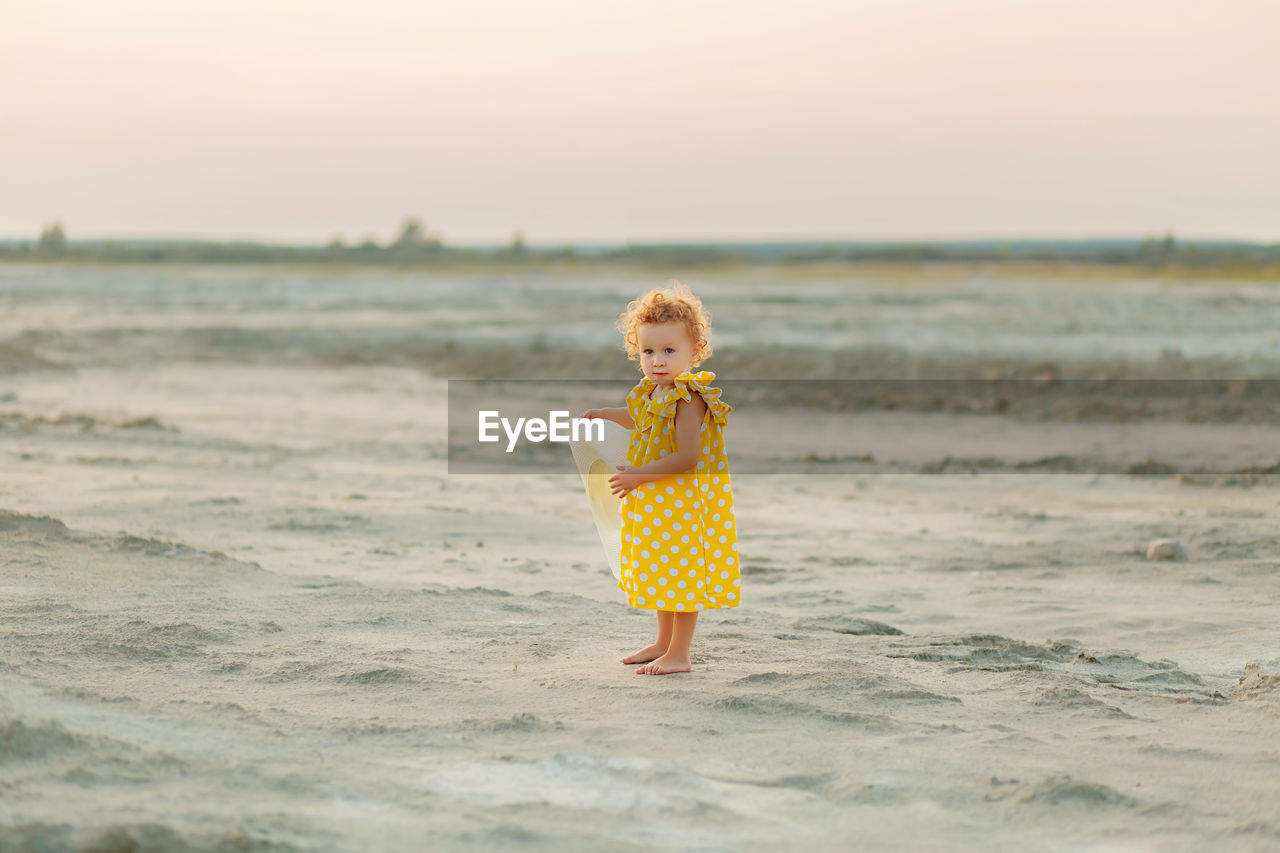 Girl standing on beach against sky during sunset