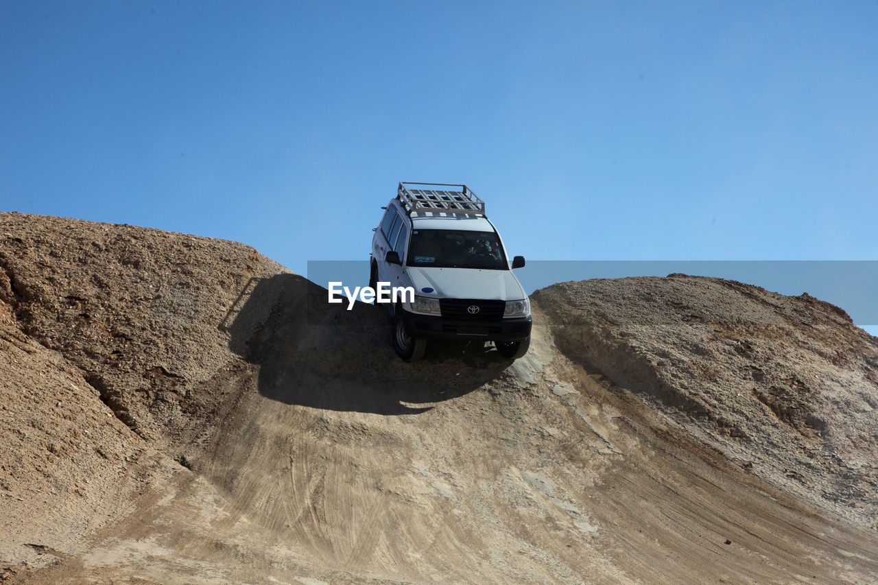 VEHICLE ON DIRT ROAD AGAINST CLEAR BLUE SKY