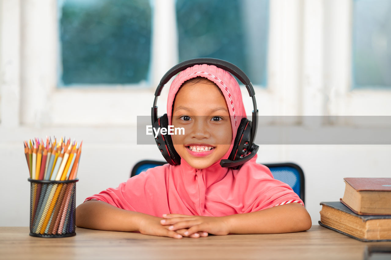 PORTRAIT OF CUTE SMILING GIRL SITTING ON TABLE