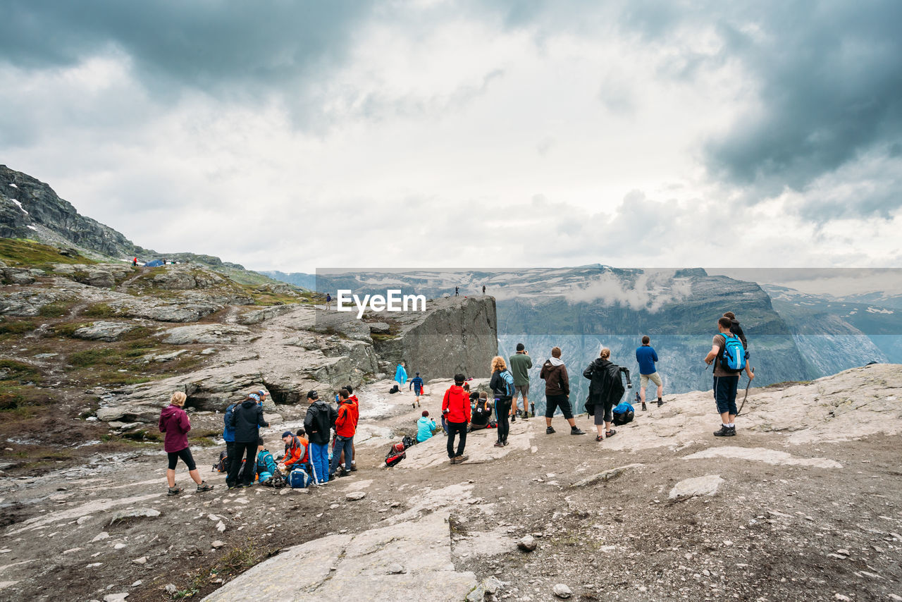 People on cliff mountain against cloudy sky