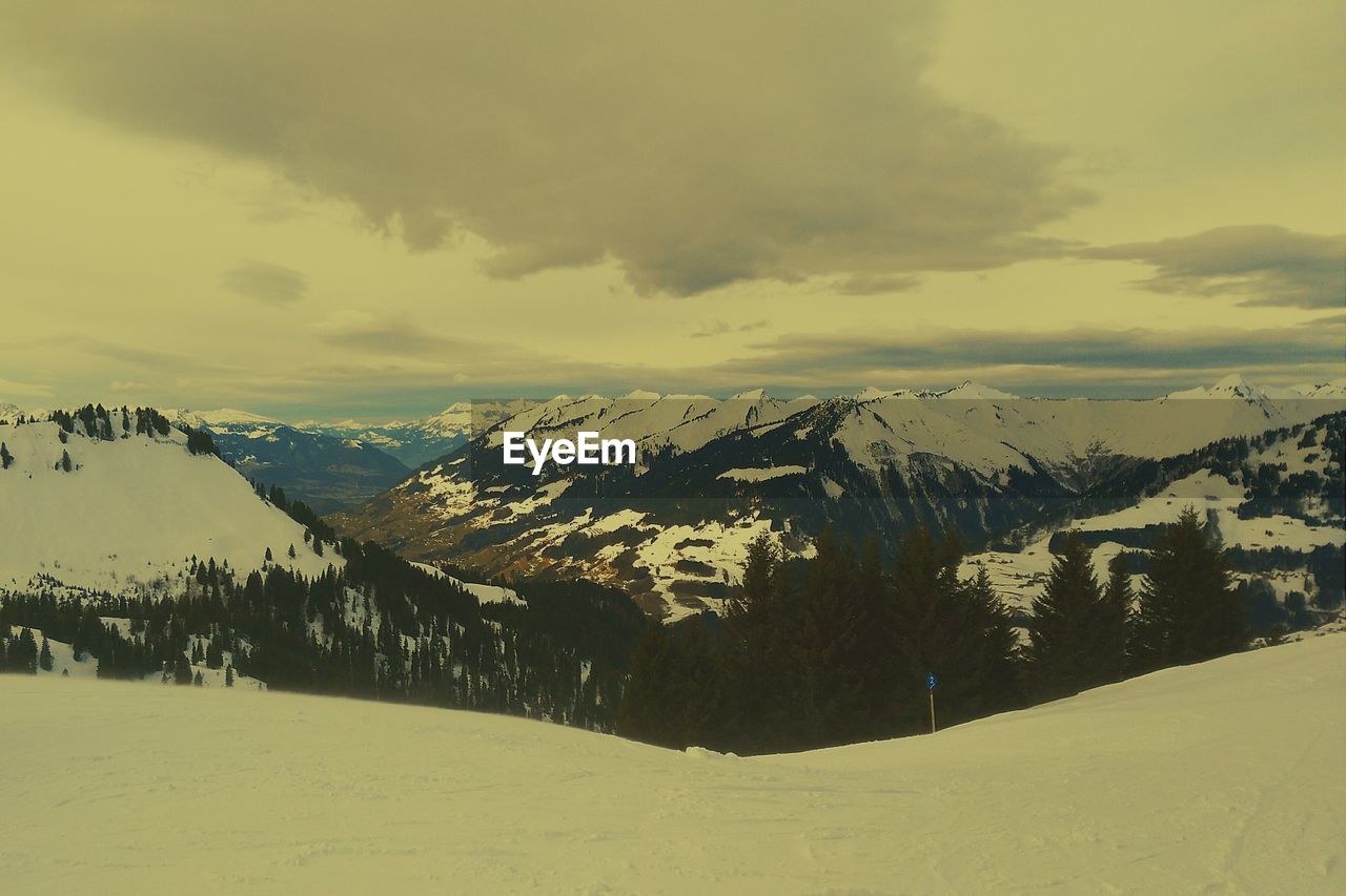 Scenic view of snow covered mountains against cloudy sky