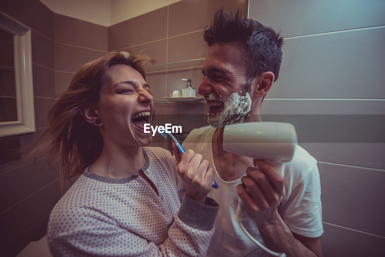 Smiling young woman with man holding toothbrush in bathroom at home