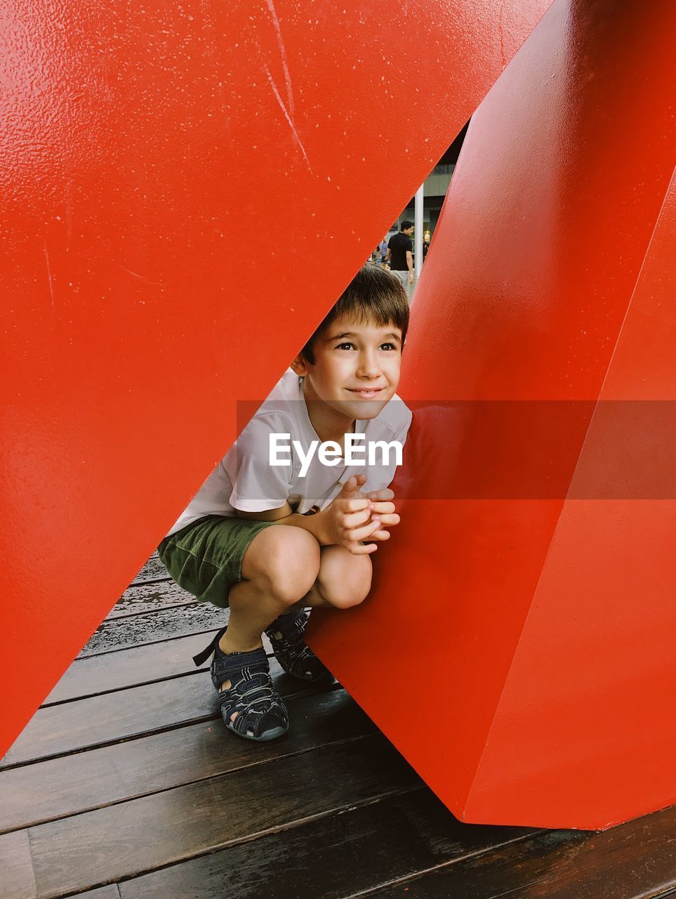 Playful boy crouching amidst red built structure