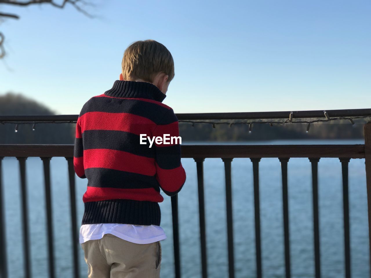 REAR VIEW OF BOY STANDING BY RAILING AGAINST BRIDGE