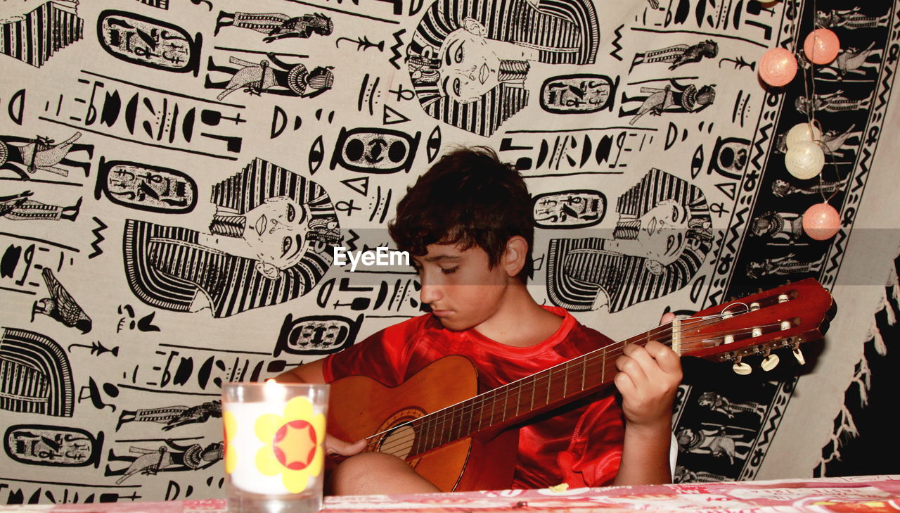 A caucasian boy plays guitar by during an evening camping on the beach