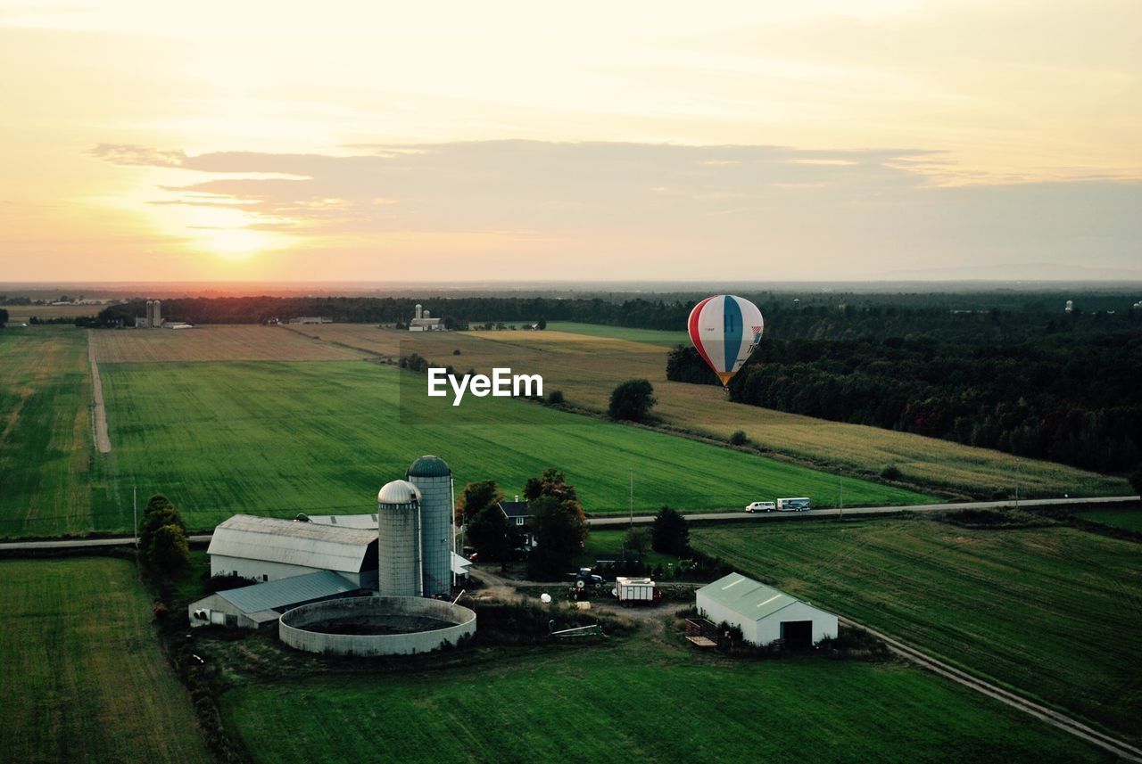 High angle view of hot air balloon over green landscape against cloudy sky during sunset