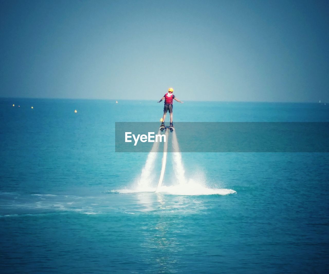 Rear view of person flyboarding at sea against blue sky