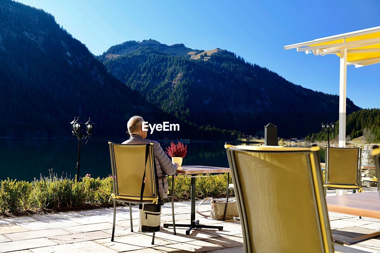 Rear view man sitting on chair by mountain range
