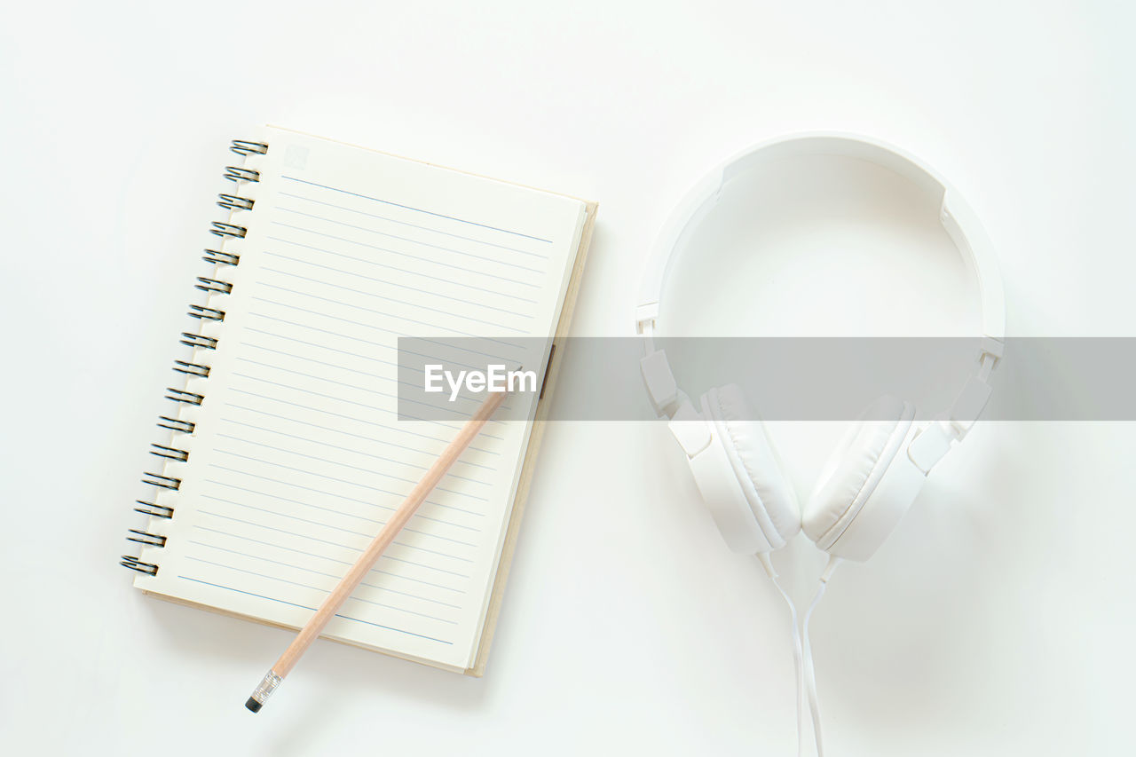 Directly above shot of headphones by spiral notebook and pencil against white background