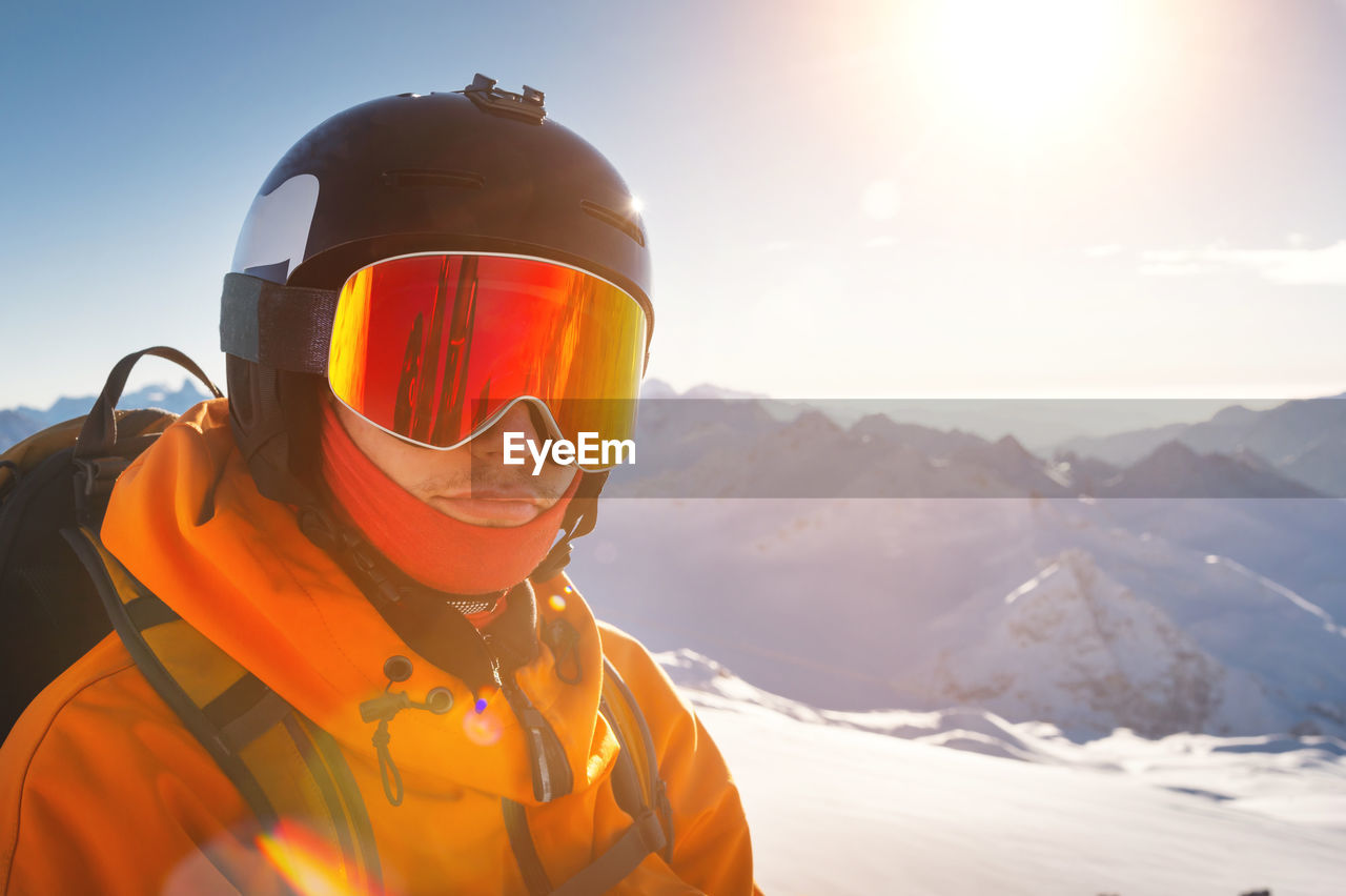 Young man in ski goggles and a helmet on a sunny snowy ski slope. portrait of a confident sportsman