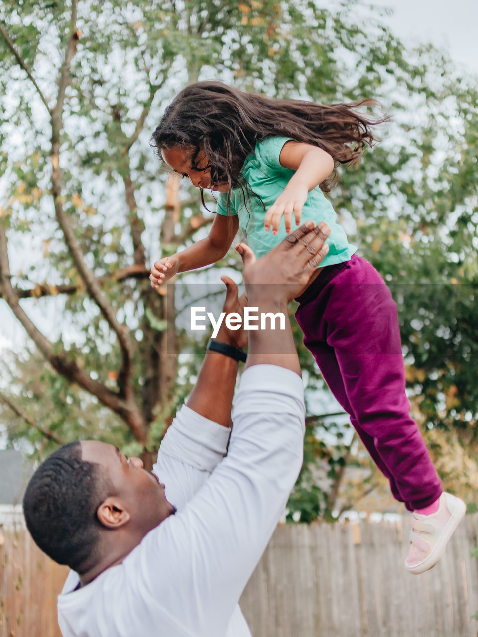 Black or african american father in white shirt in the back yard playing with mixed race daughter