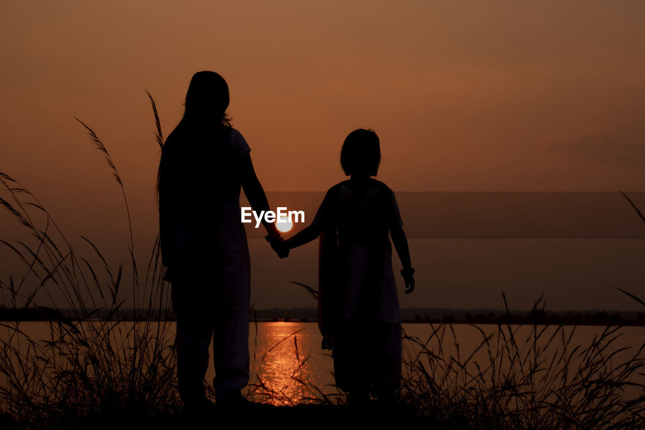 SILHOUETTE MEN STANDING ON FIELD AGAINST ORANGE SKY