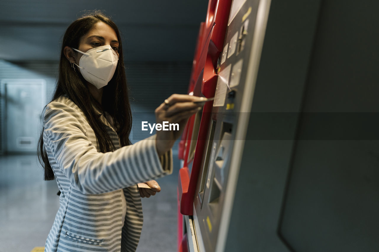 Female passenger with face mask buying ticket from kiosk during covid-19