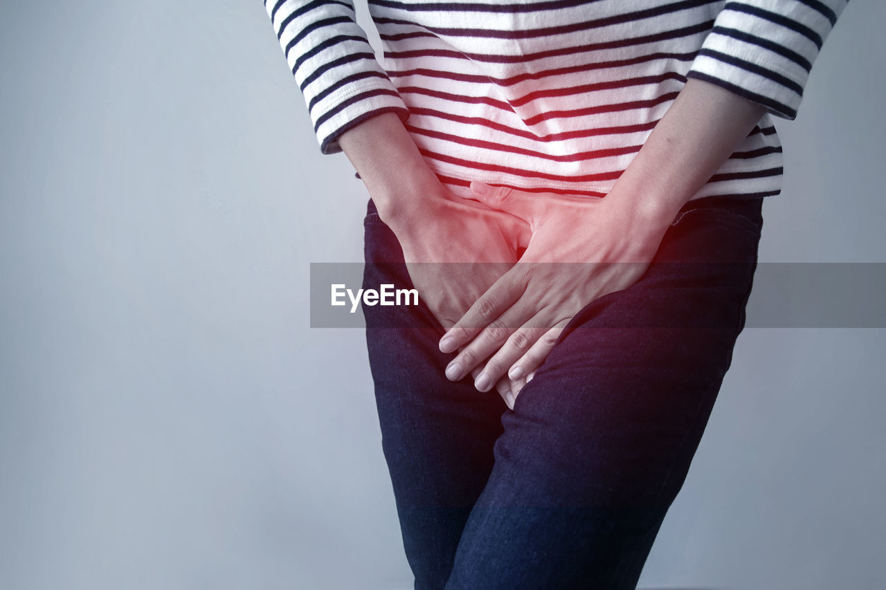 Midsection of woman with stomachache standing against gray background