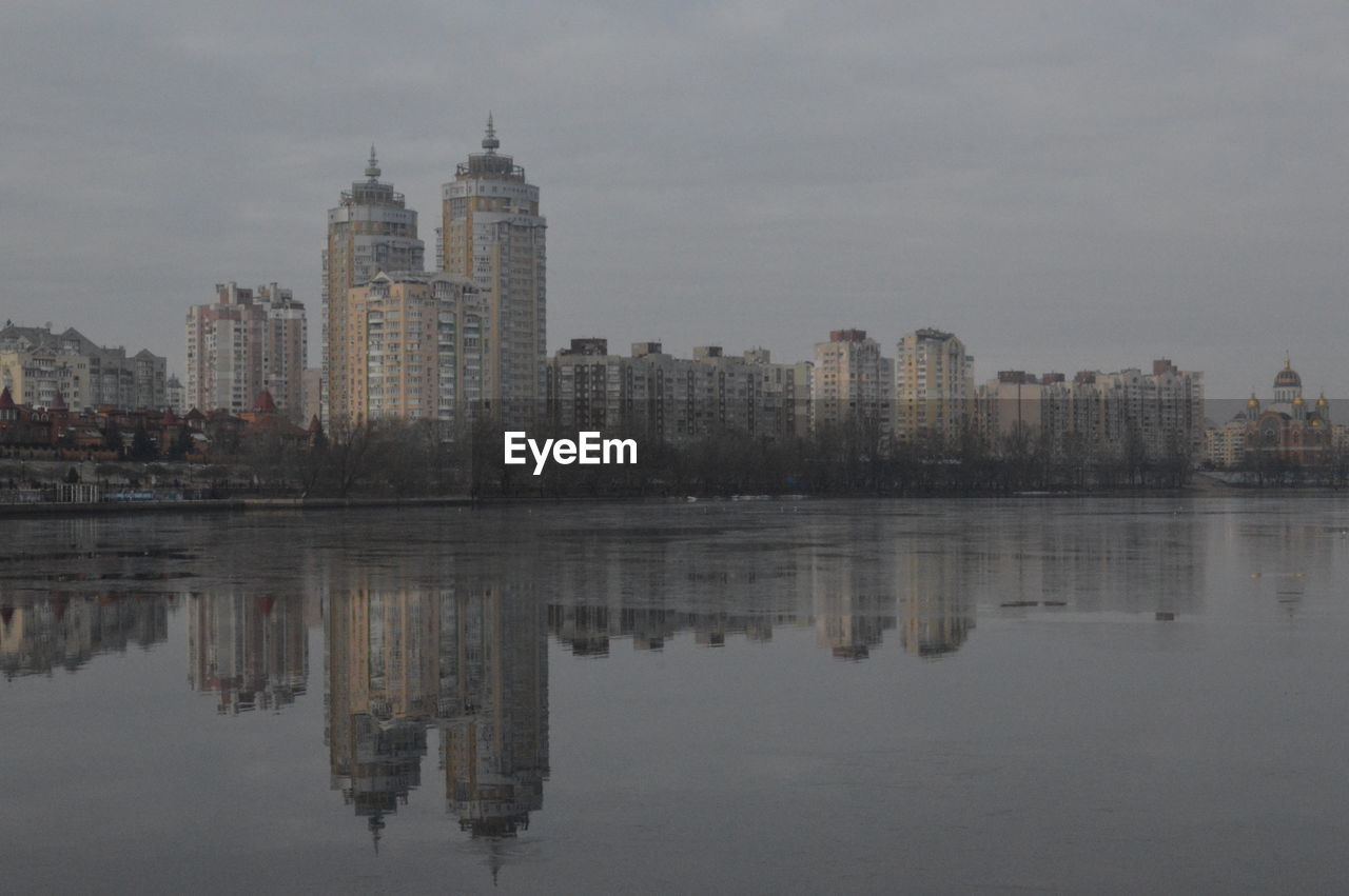 REFLECTION OF BUILDINGS IN LAKE AGAINST SKY