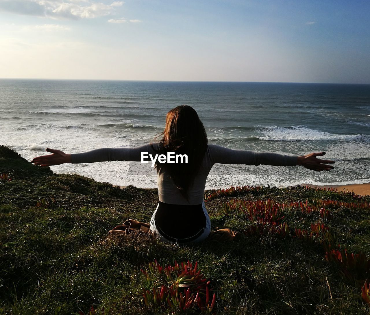 Rear view of woman arms outstretched on cliff by sea