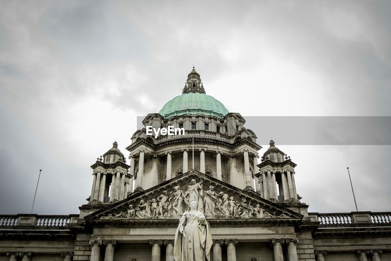 Low angle view of statue and belfast city hall against cloudy sky