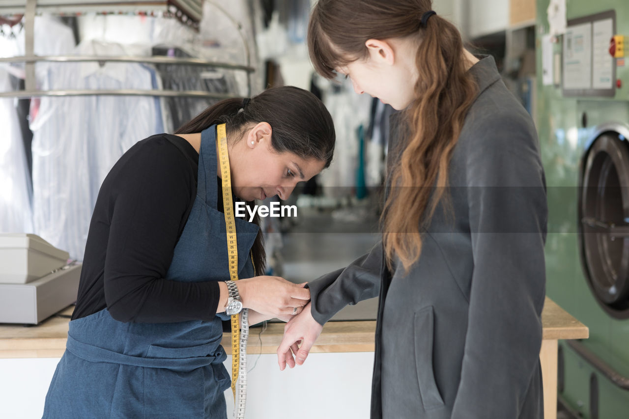 Side view of mature female tailor adjusting overcoat sleeve for young customer