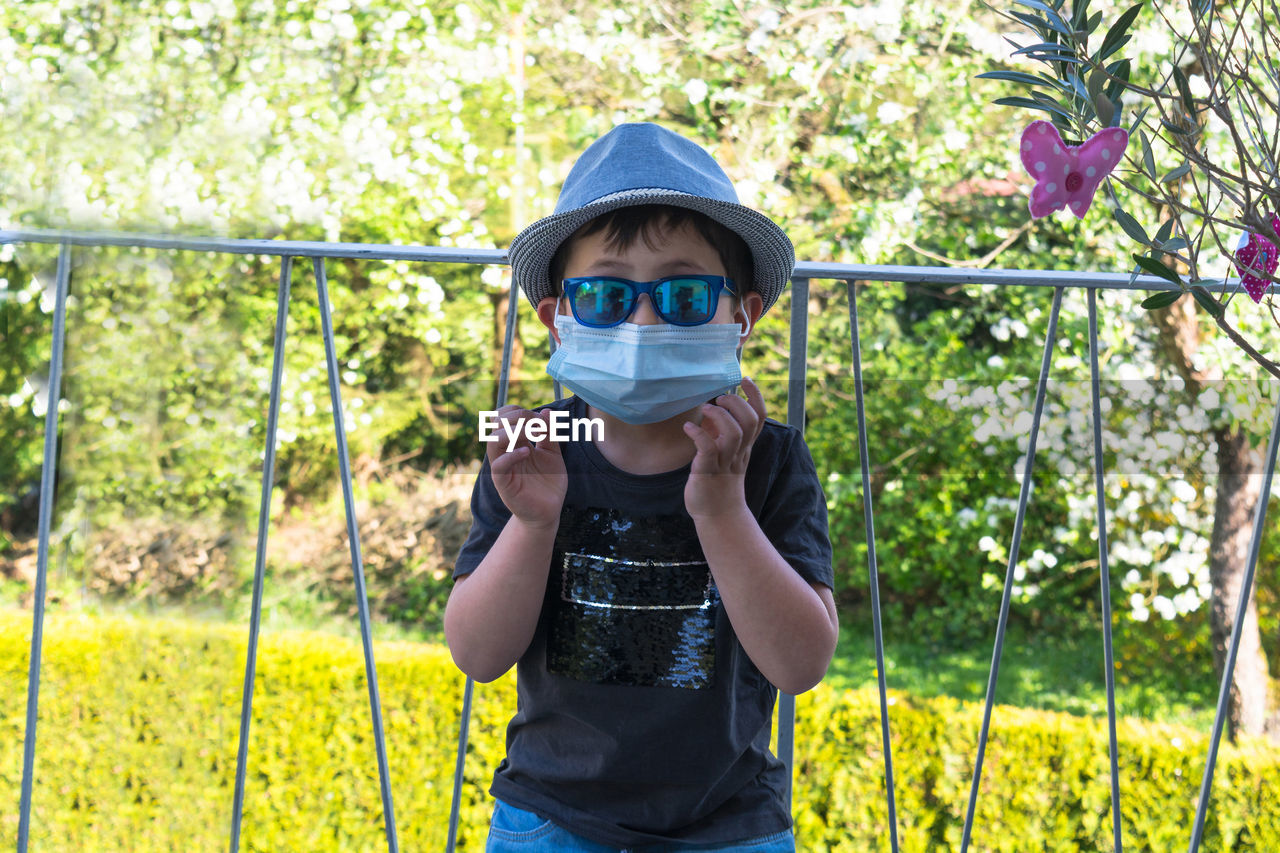 Portrait of boy wearing surgical mask while standing against railing