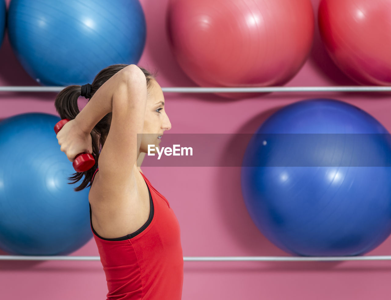 Side view of woman lifting dumbbell against fitness balls