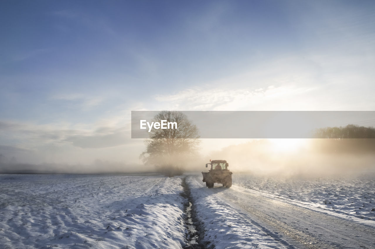 Vehicle on snow covered road against sky during sunset