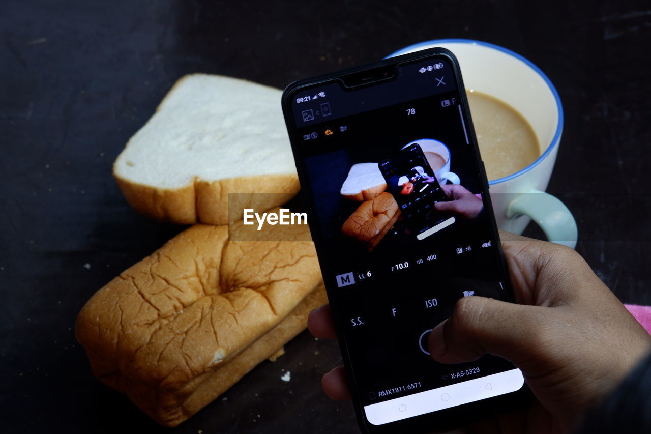 CLOSE-UP OF HAND HOLDING CAMERA AND MOBILE PHONE IN CONTAINER