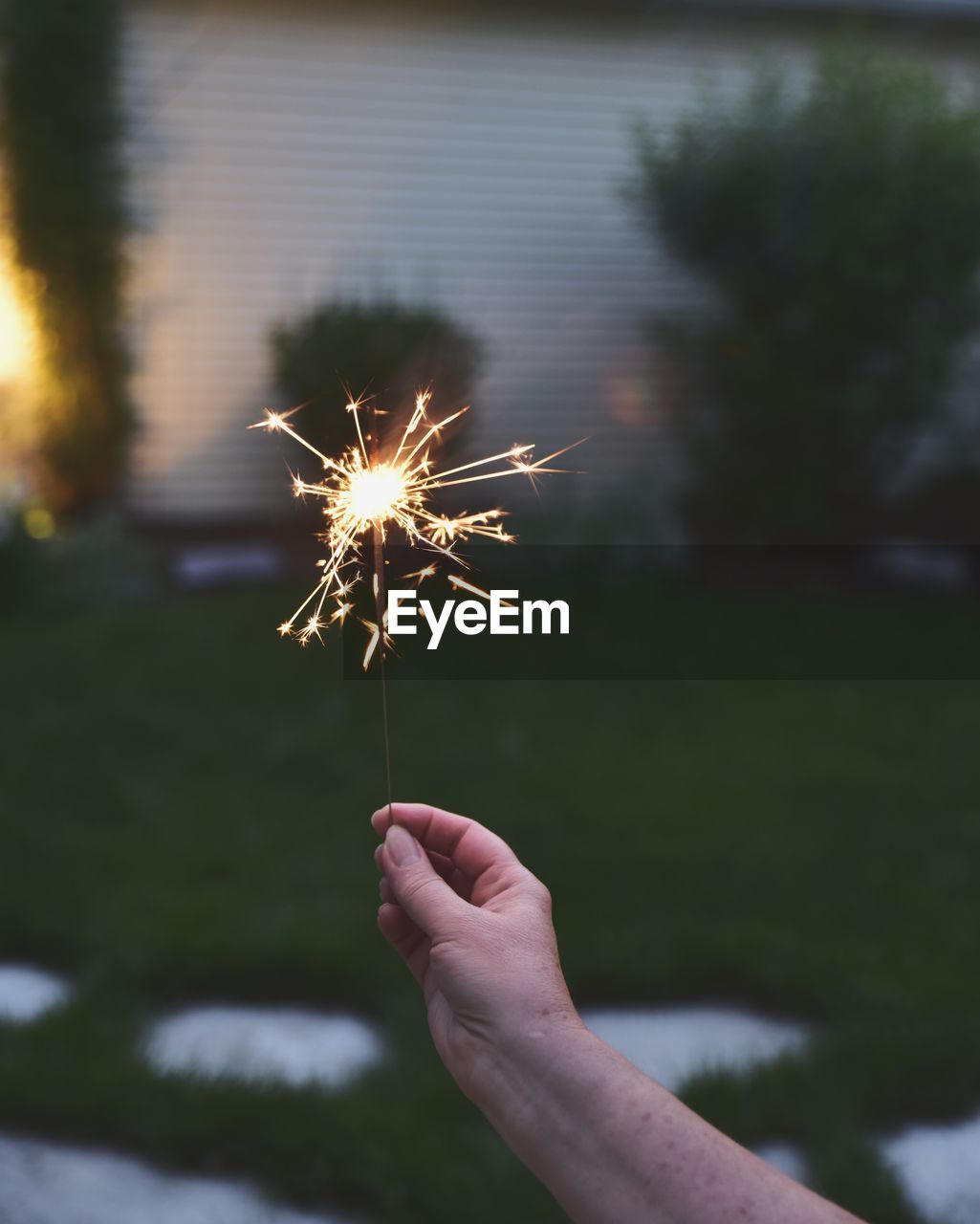 Cropped image of woman hand holding sparkler at dusk