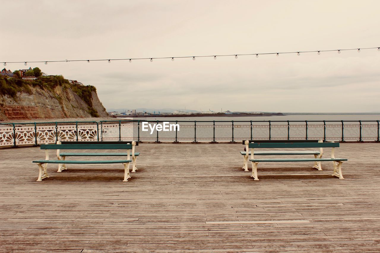 EMPTY BENCH BY RAILING AGAINST SKY