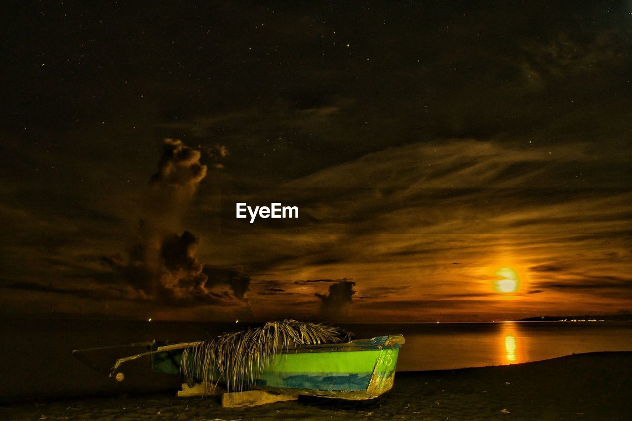 Boats moored on shore against sky during sunset