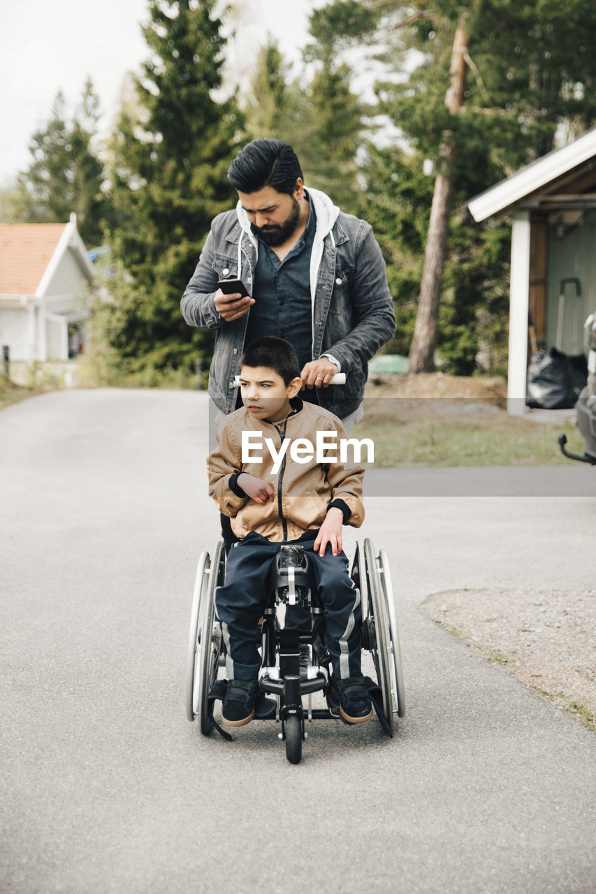 Father using smart phone while pushing autistic son on wheelchair