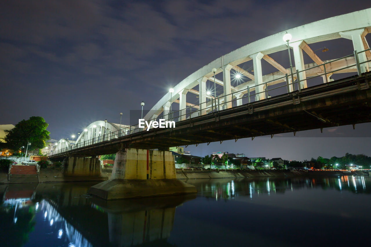 LOW ANGLE VIEW OF BRIDGE OVER RIVER AGAINST SKY IN CITY AT NIGHT