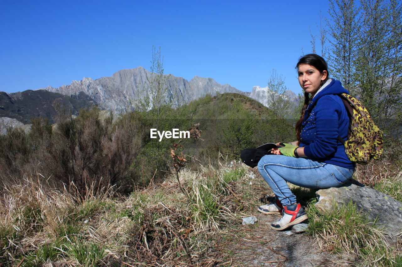 FULL LENGTH OF MAN SITTING ON ROCKS AGAINST MOUNTAINS