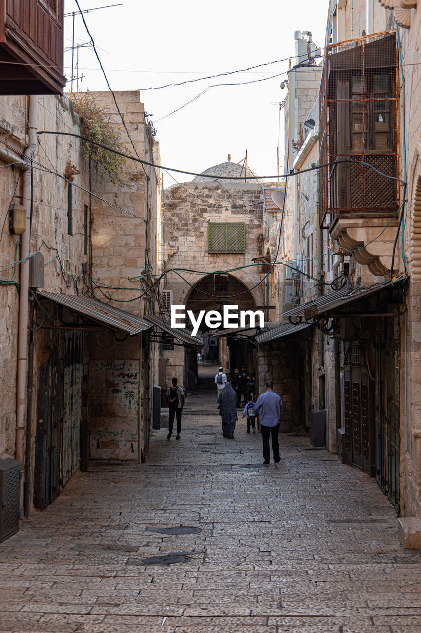 PEOPLE WALKING ON ALLEY AMIDST BUILDINGS IN CITY