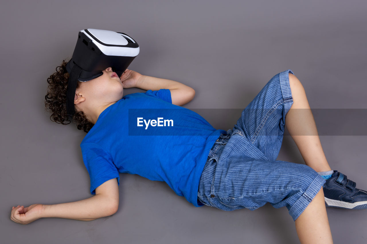 Photo of child playing with virtual reality glasses. lying on the ground