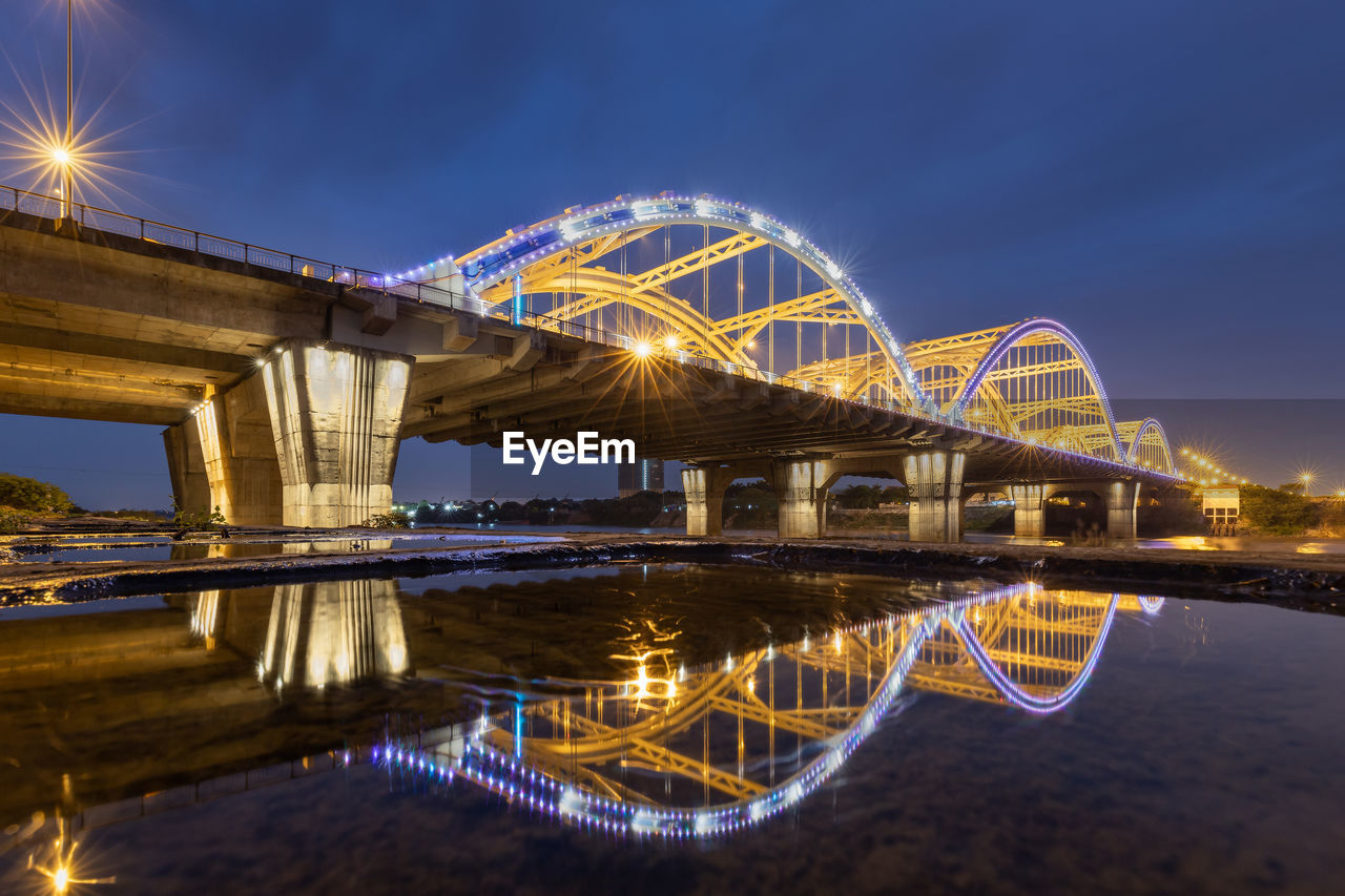 Illuminated bridge over river against sky at night