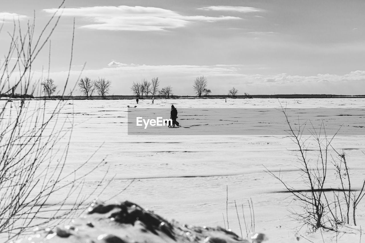 winter, snow, cold temperature, nature, black and white, water, sky, one person, land, monochrome photography, beauty in nature, day, scenics - nature, leisure activity, environment, monochrome, landscape, skiing, cloud, non-urban scene, vacation, lifestyles, full length, holiday, white, tranquility, trip, beach, men, tranquil scene, outdoors, sports, sea, winter sports, activity, mountain, plant, frozen, adult, travel, animal, adventure