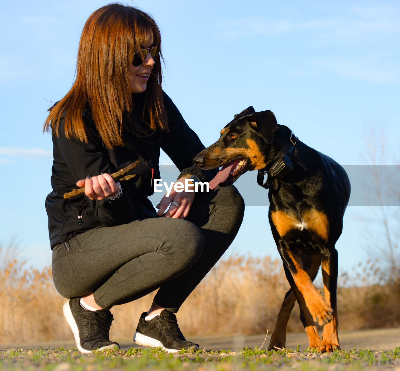 YOUNG WOMAN WITH DOG SITTING ON FIELD