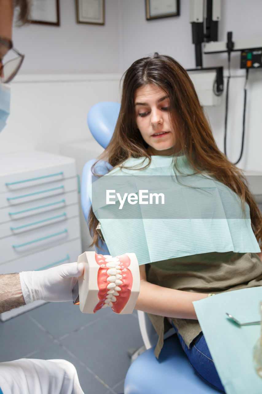 Professional doctor demonstration process of healthy teeth brushing to young woman sitting in chair.