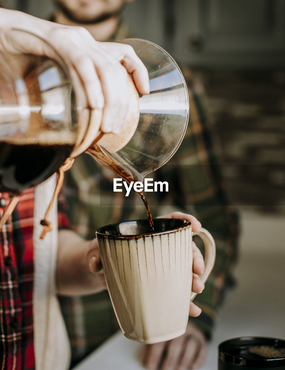 Hot coffee is poured from a pour over into a tan coffee cup