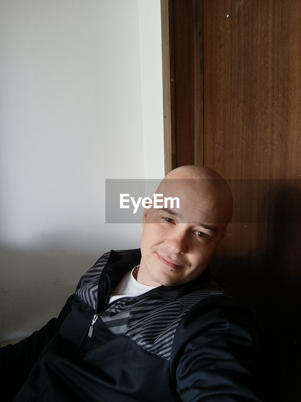 one person, portrait, black, adult, indoors, shaved head, men, emotion, person, waist up, headshot, looking at camera, copy space, lifestyles, sitting, front view, completely bald, clothing, relaxation, mature adult, human face, smiling, home interior
