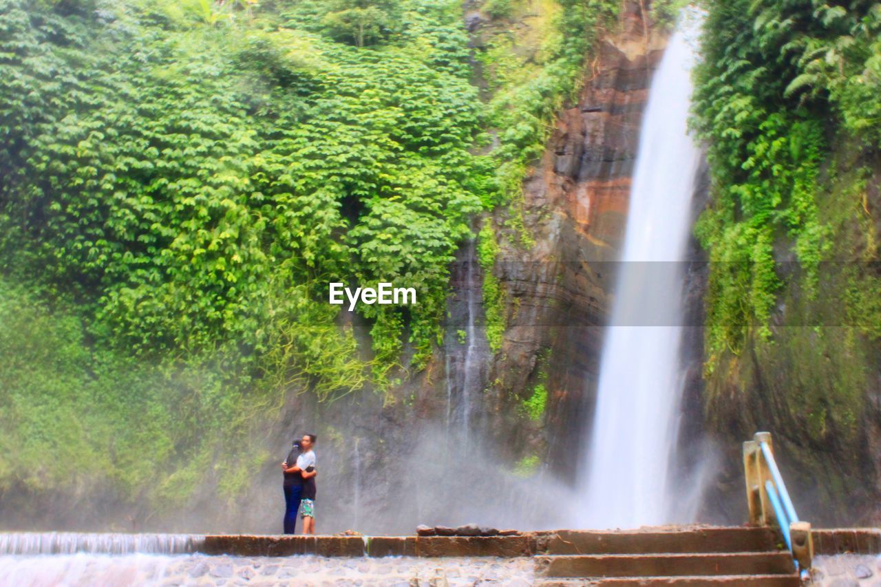 MAN STANDING BY WATERFALL