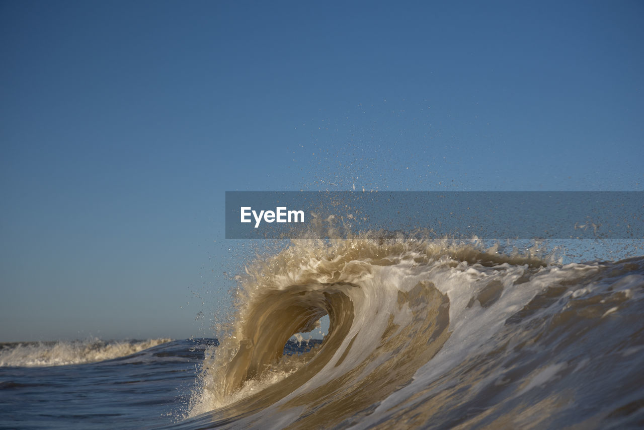 Waves splashing in sea against clear blue sky