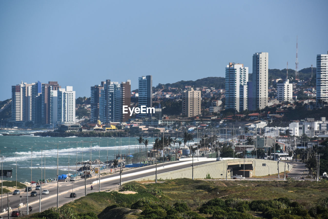 Cityscape by sea against clear sky