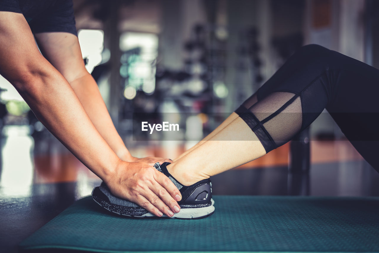 Cropped hands of trainer holding woman leg during exercise in gym